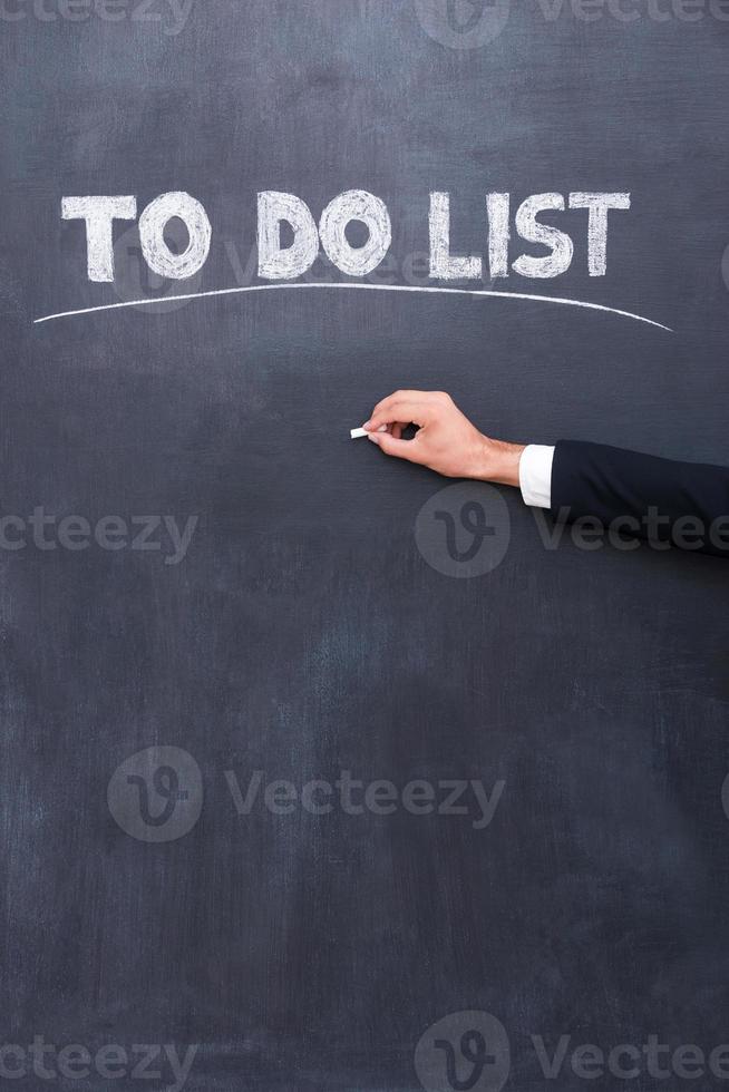 To do list. Close-up of human hand writing to do list on the blackboard photo