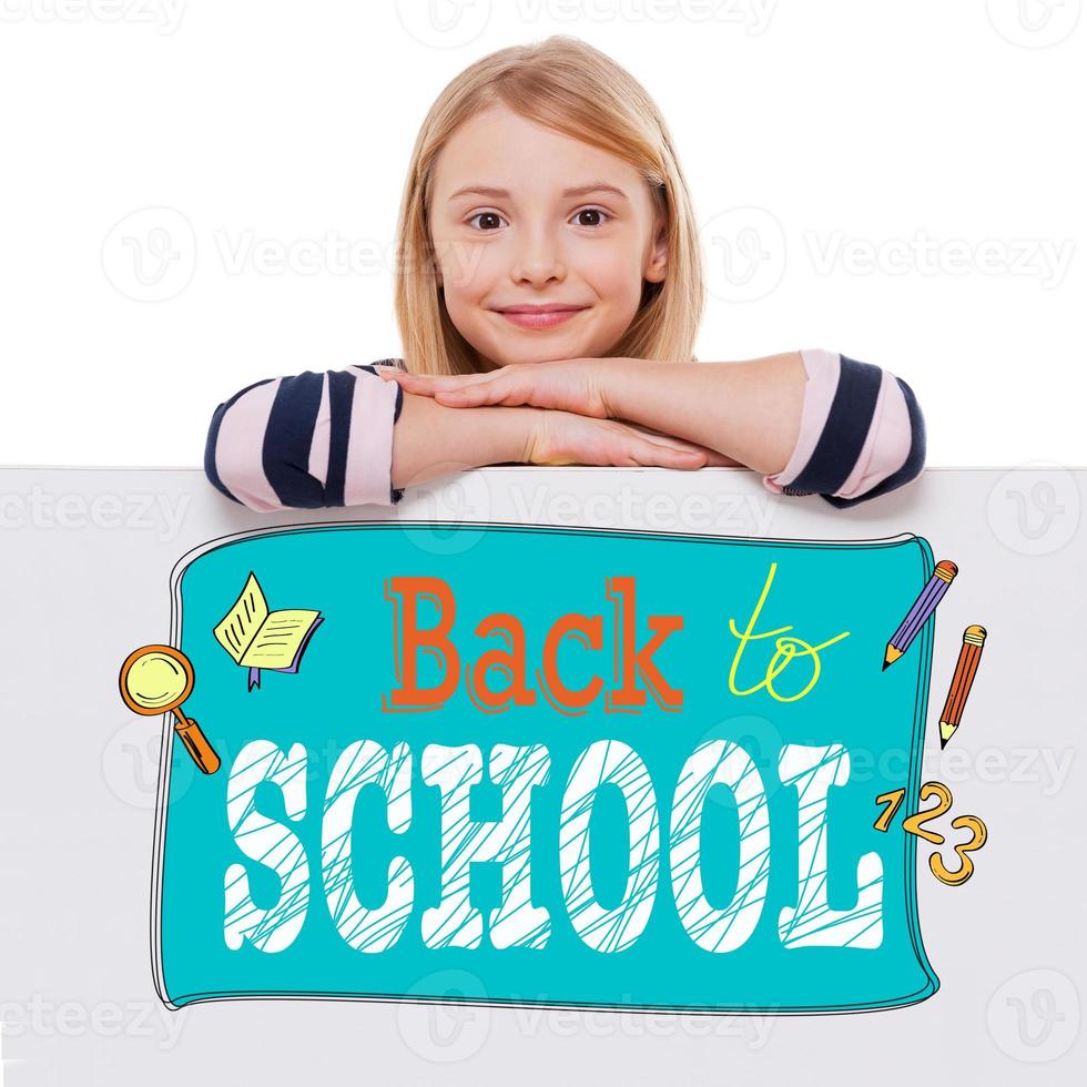 Back to school. Cheerful girl leaning over white board with sketch on it and looking at camera with smile while standing against white background photo
