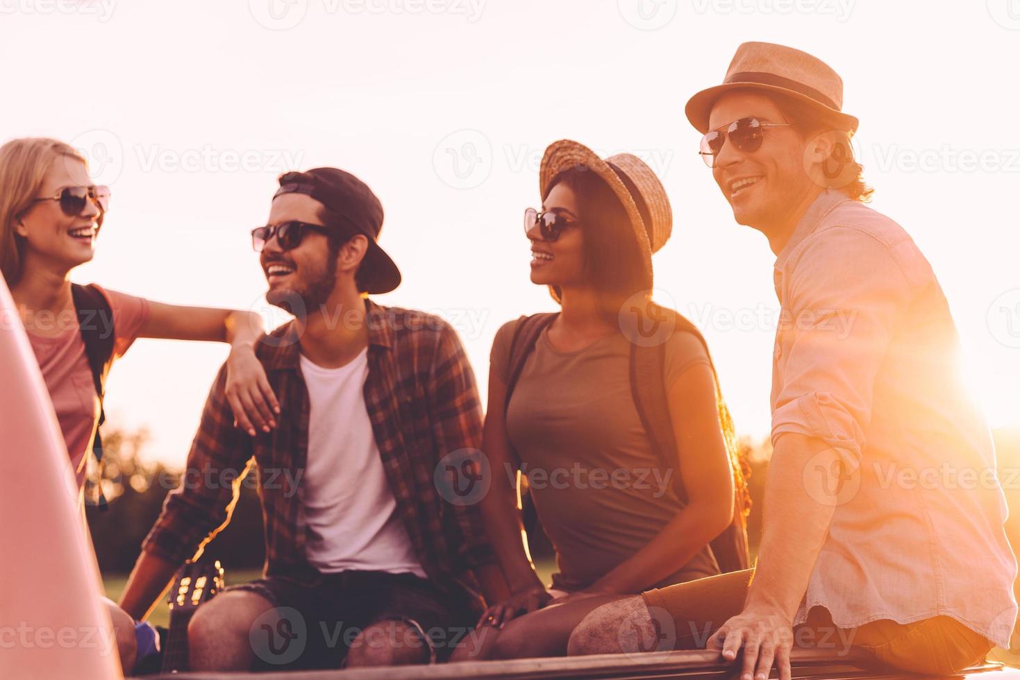 Road trip with best friends. Group of young cheerful people enjoying their road trip while sitting in pick-up truck together photo