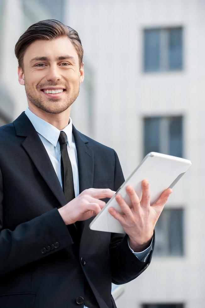Successful businessman. Cheerful young men in formalwear holding digital tablet and looking at camera photo
