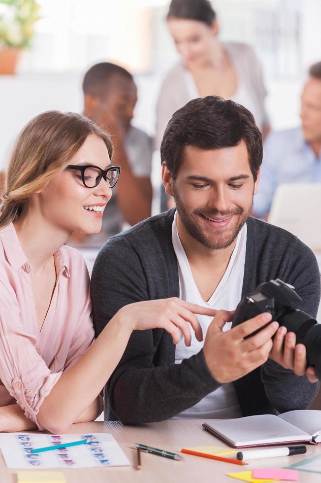 Discussing shots. Two co-workers holding camera and smiling while three people working on background photo