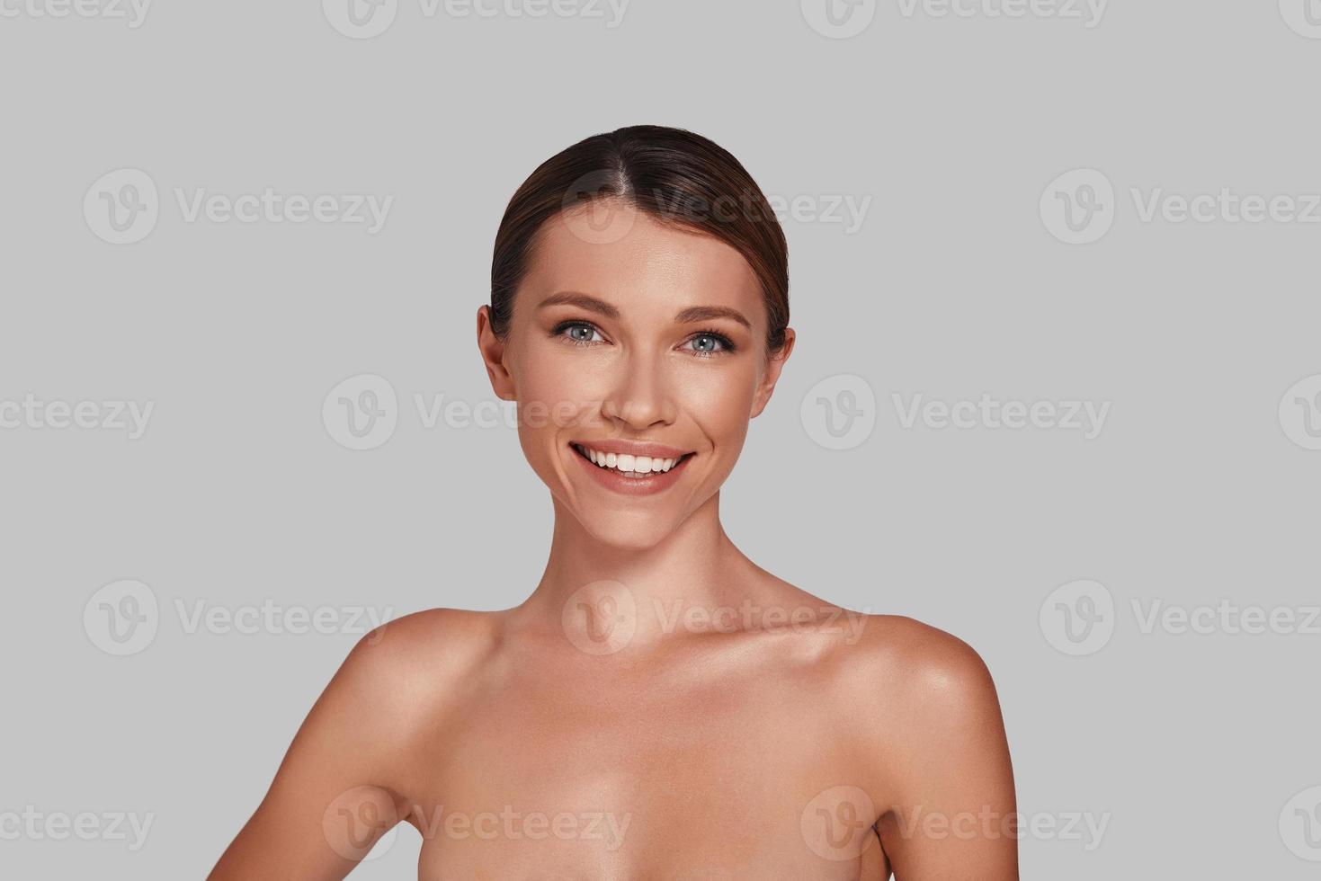 Gorgeous beauty. Attractive young woman looking at camera and smiling while standing against grey background photo
