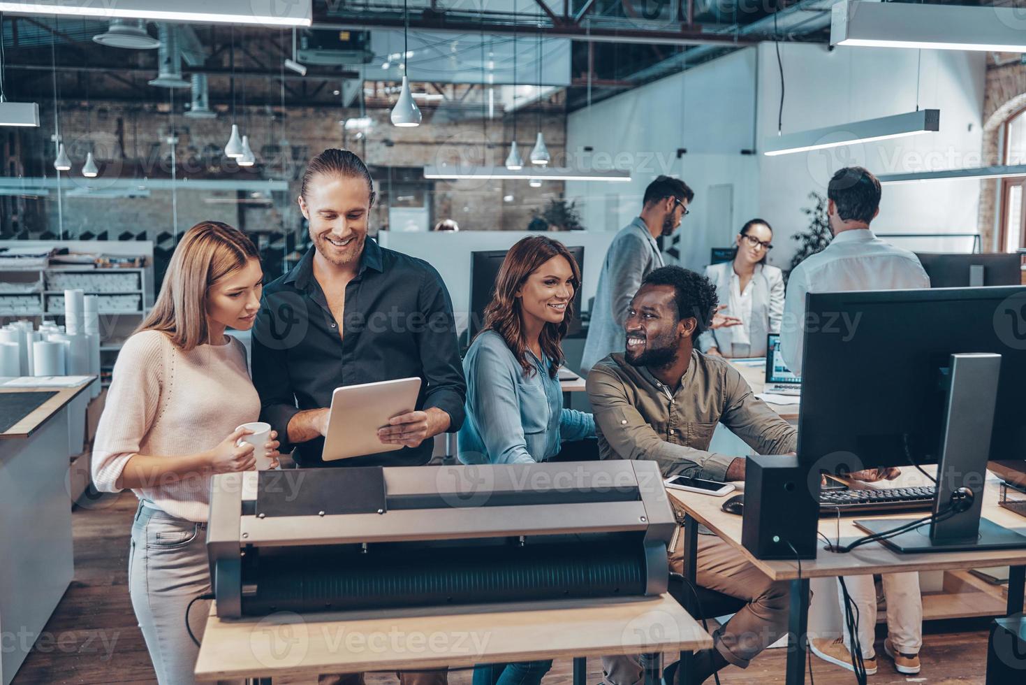 Group of young modern people in smart casual wear communicating and using modern technologies while working in the office photo