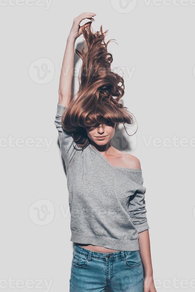 Confident in her healthy hair. Attractive young woman stretching her hair up and while standing against grey background photo