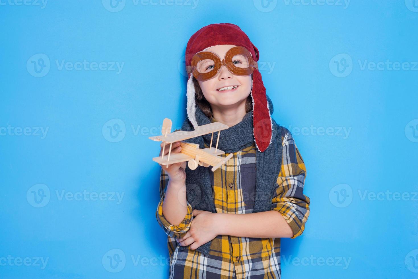 Dreaming of a big sky. Thoughtful of little boy in helmet playing with toy plane while standing against blue background photo