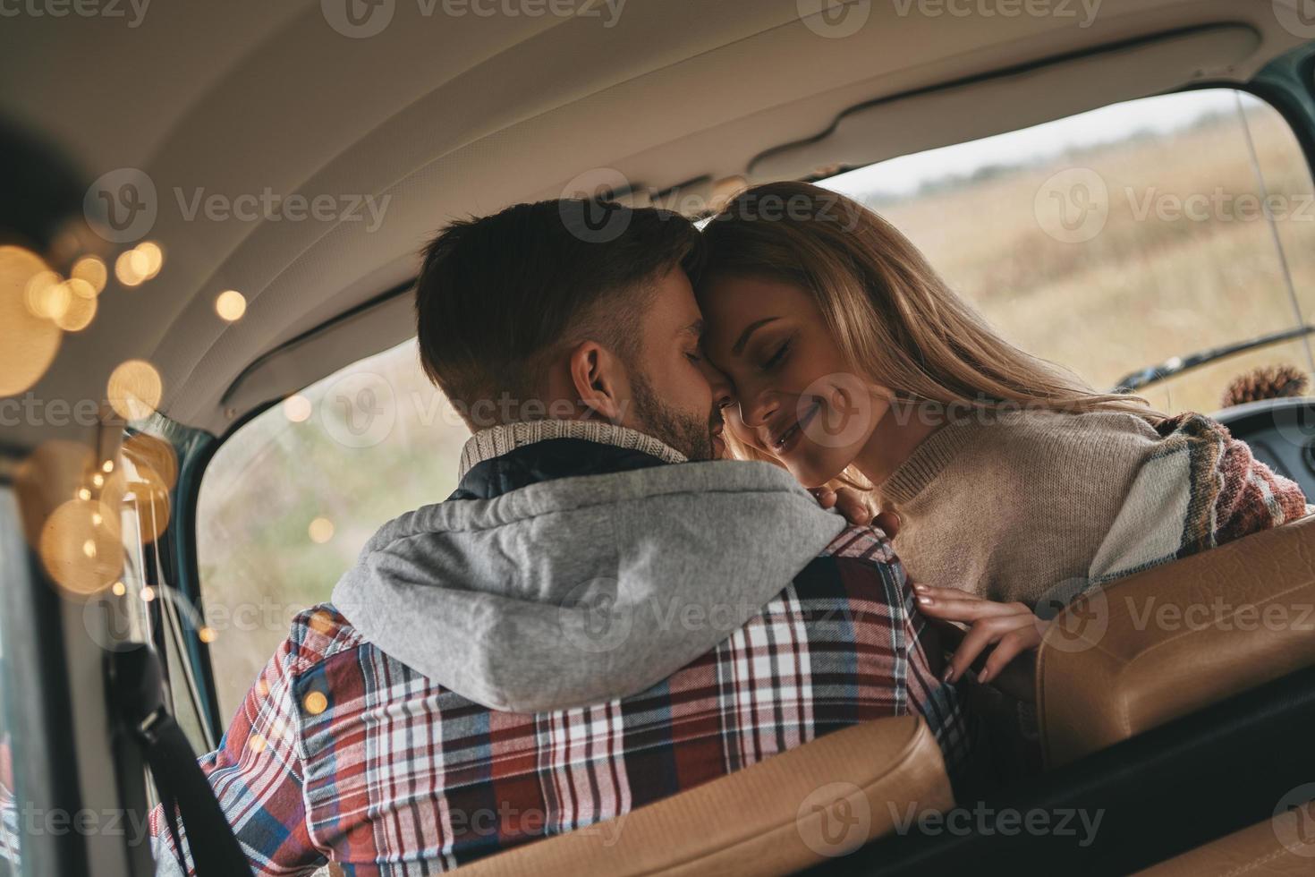 He will never let her go. Beautiful young couple smiling while sitting face to face on the front passenger seats in retro style mini van photo