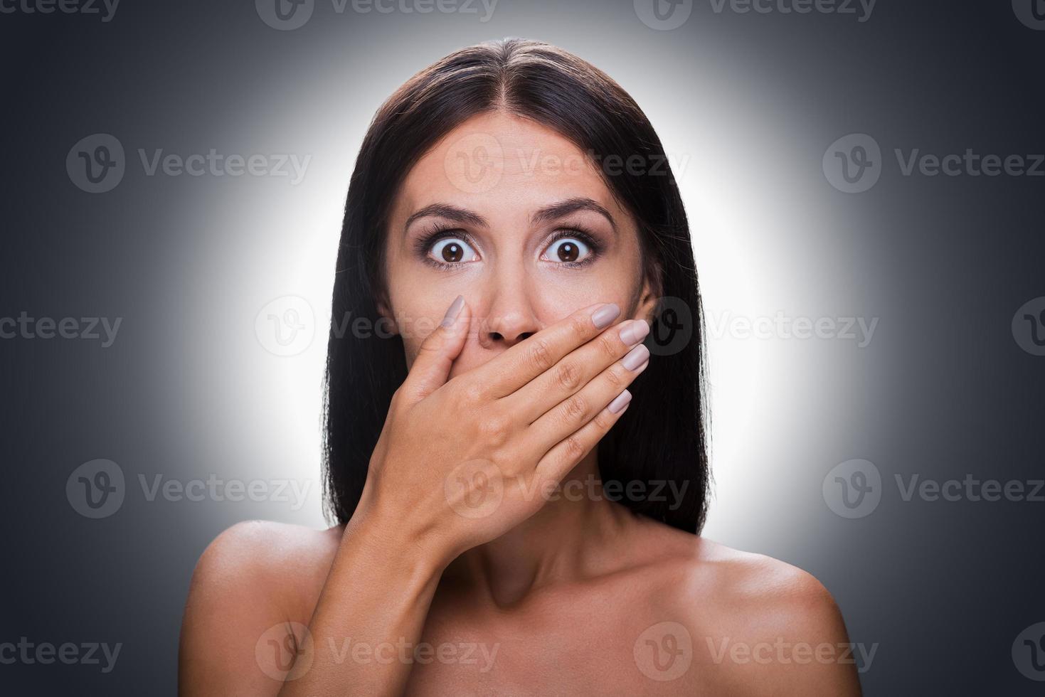 No more word Portrait of shocked young shirtless woman looking at camera and covering mouth by hand while standing against grey background photo