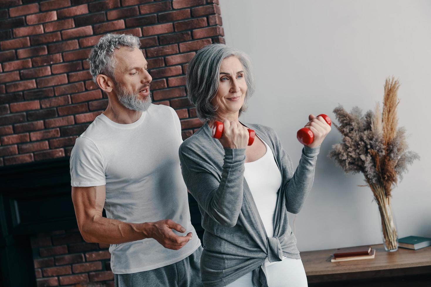 Modern senior couple in sports clothing exercising and using hand weight while spending time at home photo