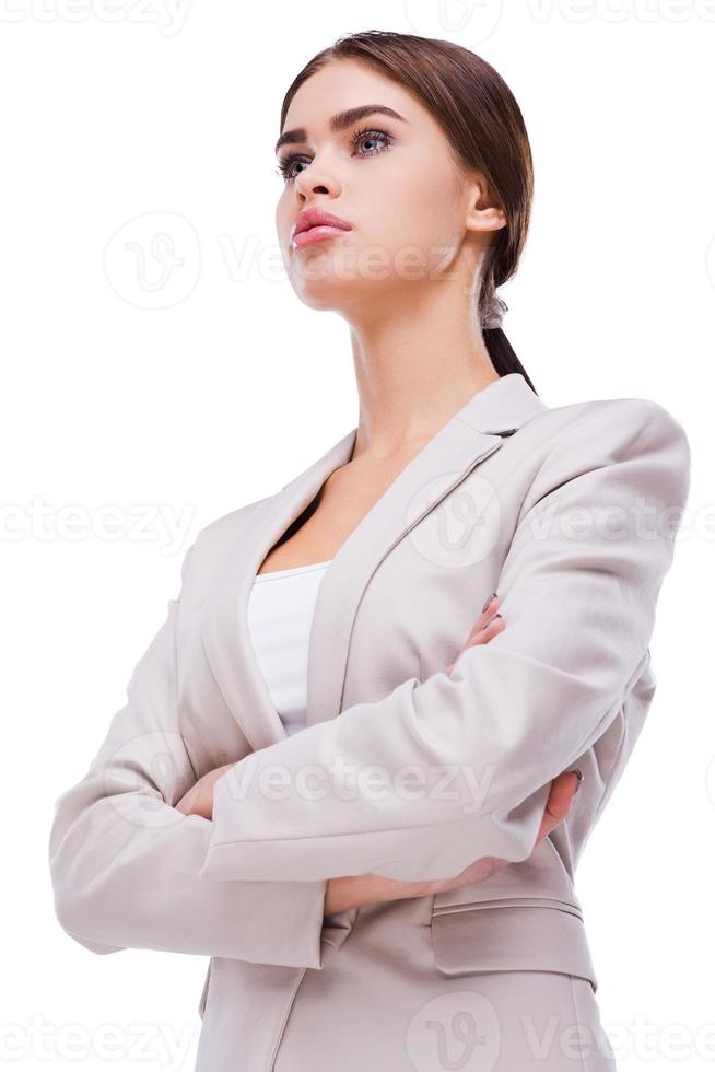 Confident businesswoman. Low angle view of confident young businesswoman keeping arms crossed while standing against grey background photo