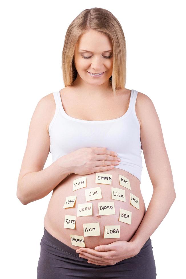 Choosing name for a baby. Beautiful pregnant woman looking at the adhesive notes with baby names and smiling while standing isolated on white photo