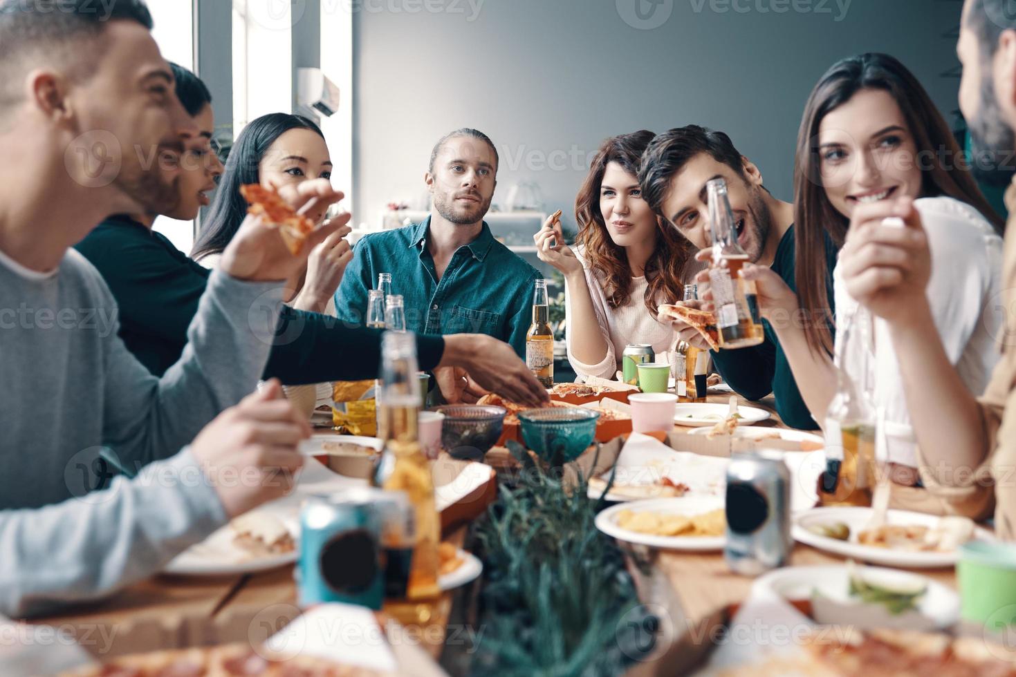 Meeting with best friends. Group of young people in casual wear eating pizza and smiling while having a dinner party indoors photo