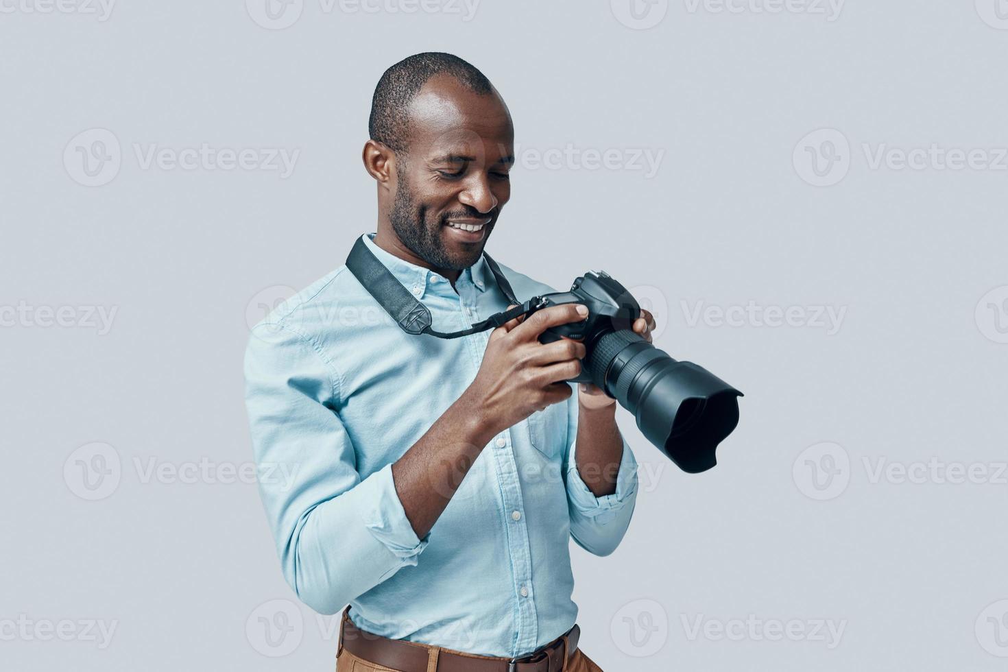 feliz joven africano usando una cámara digital y sonriendo mientras se enfrenta a un fondo gris foto