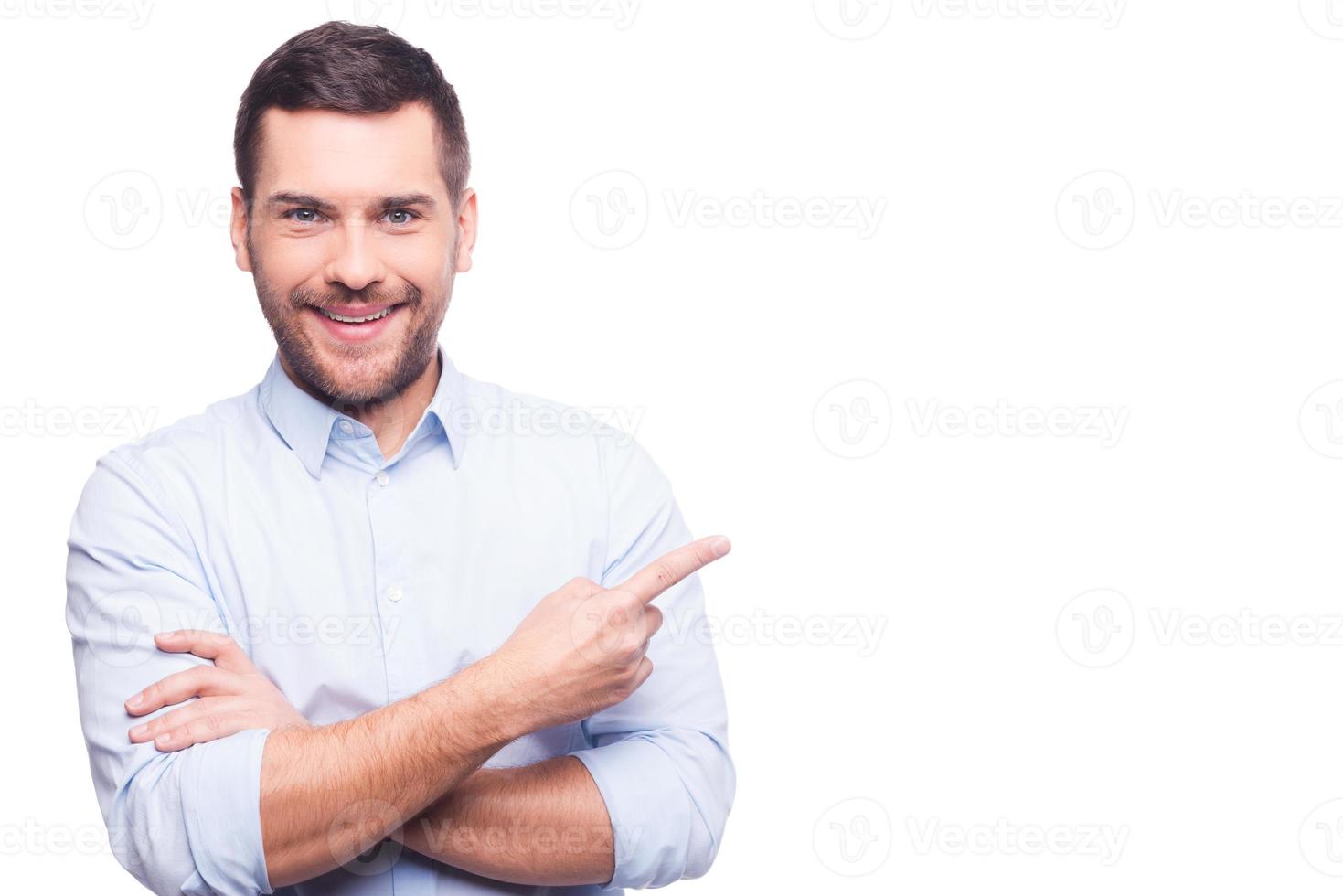 Businessman pointing copy space. Handsome young man in shirt looking at camera and pointing away while standing against white background photo