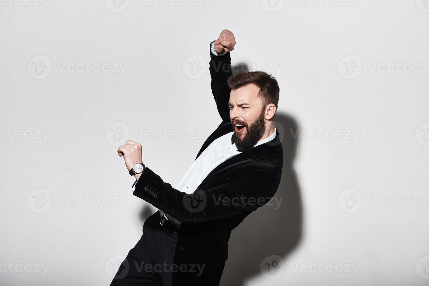 In a mood to go crazy. Handsome young man in full suit making a face and gesturing while standing against grey background photo