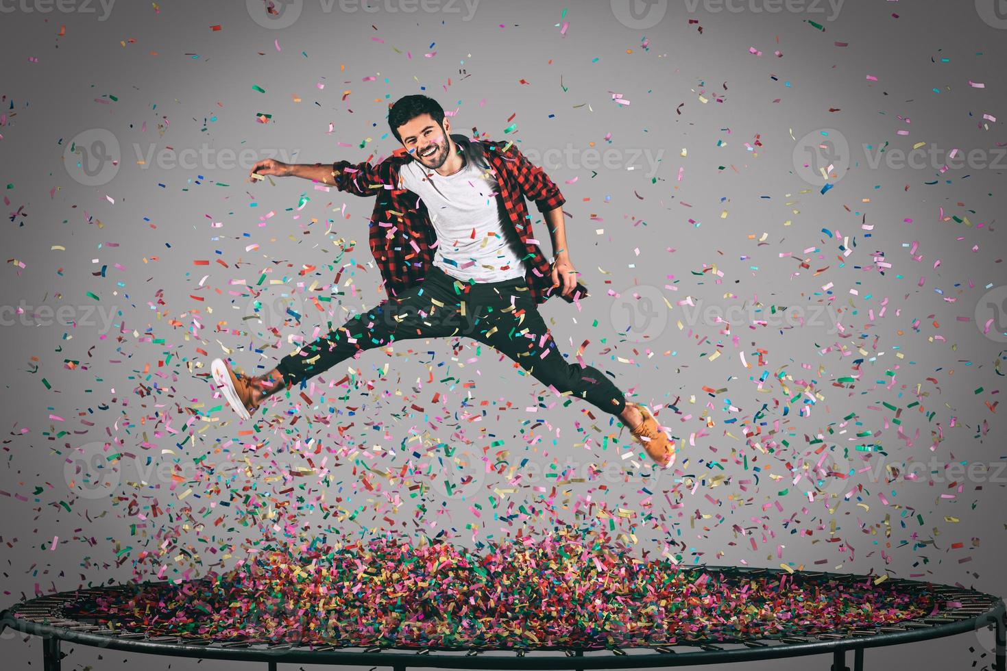 Carefree fun. Mid-air shot of handsome young man jumping on trampoline with confetti all around him photo