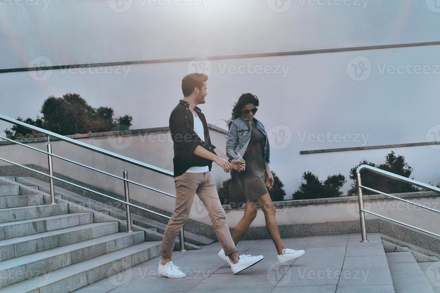 Enjoying time together. Full length of handsome man and young attractive woman holding hands while walking down the stairs outdoors photo