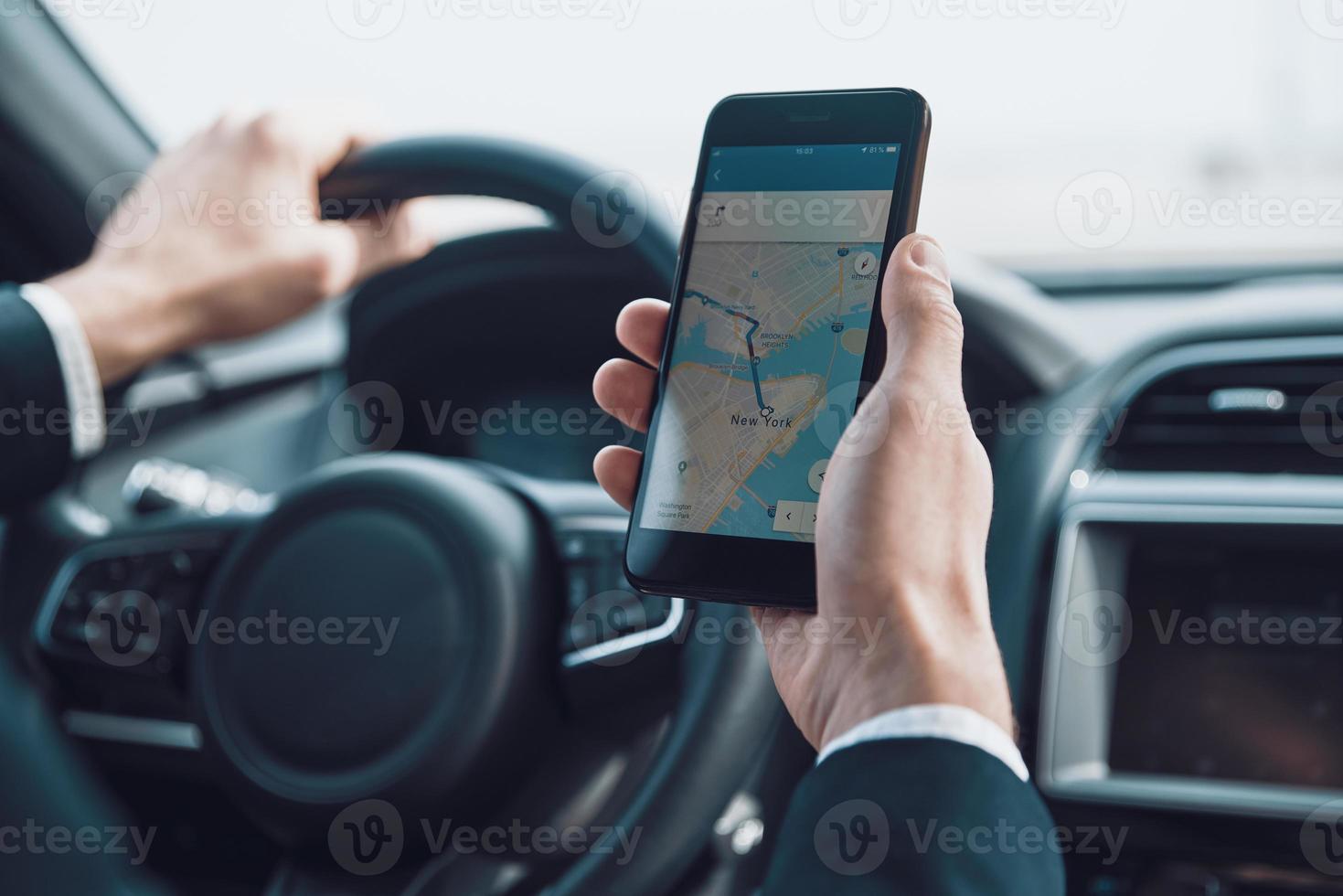 Searching for the shortest way. Close up of young man using smart phone to check the map while driving a car photo