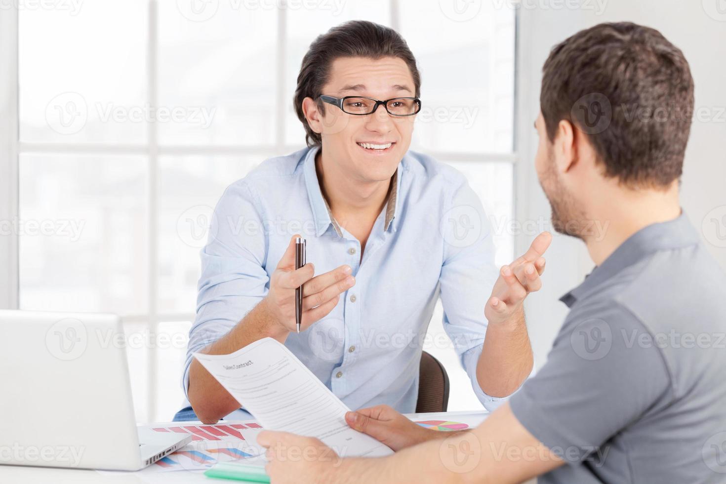 discutiendo contrato. dos alegres empresarios con ropa informal discutiendo algo y gesticulando mientras se sientan en la mesa foto