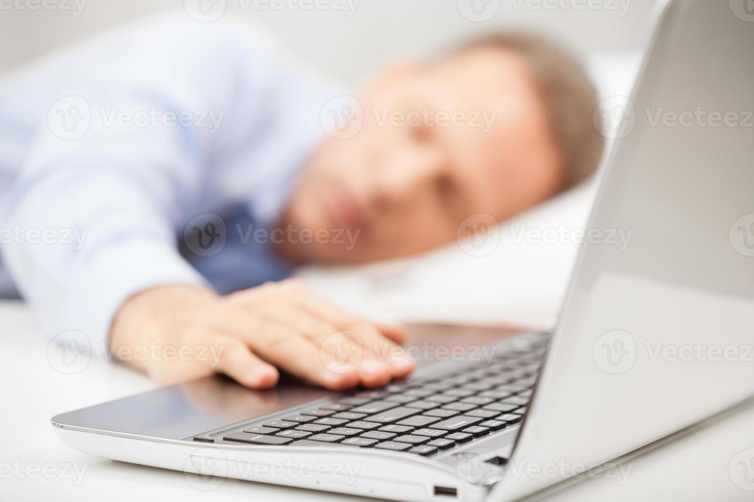 Overworked businessman. Grey hair man in formalwear holding hand on laptop keyboard while sleeping in bed photo