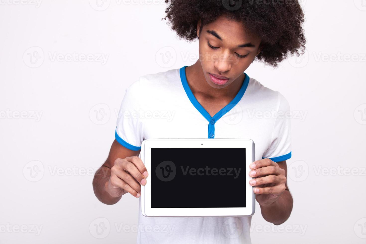 Looking at copy space. Curious African teenager on touchscreen of digital tablet while standing isolated on grey background photo