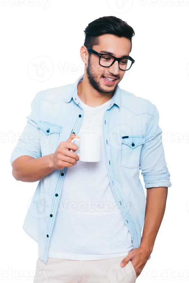 Inspired with cup of fresh coffee. Handsome young Indian man holding coffee cup and smiling while standing against white background photo