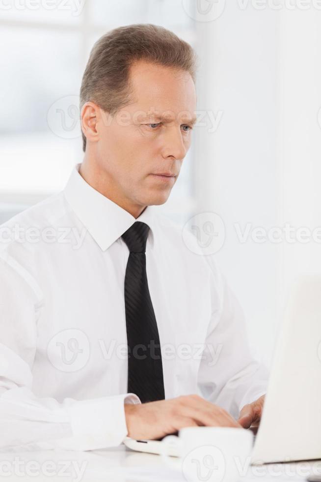 Businessman at work. Confident mature man in shirt and tie using computer while sitting at his working place photo