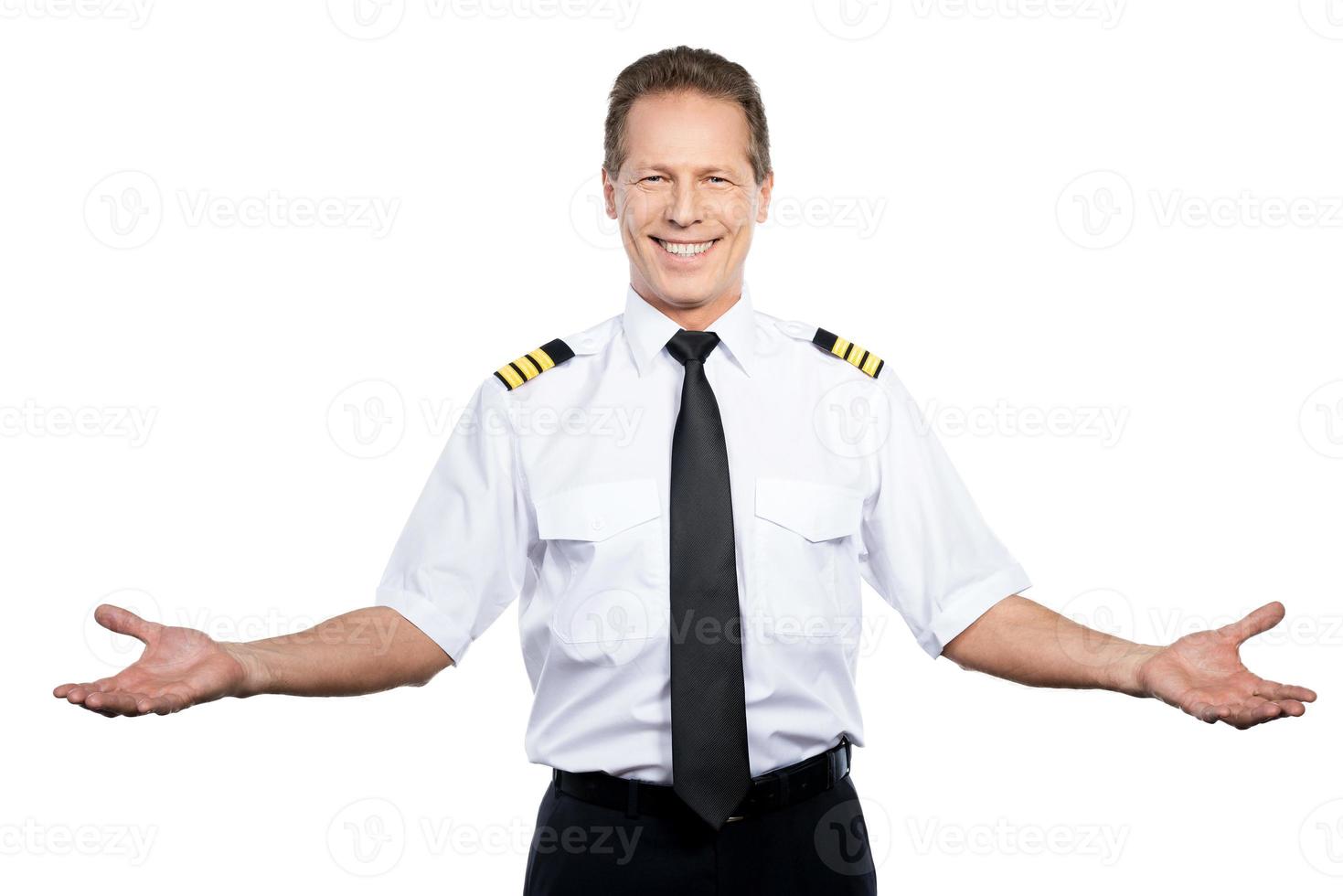 bienvenido a bordo feliz piloto masculino en uniforme gesticulando y sonriendo mientras está de pie contra el fondo blanco foto