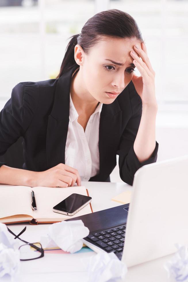 Busy office life. Frustrated young woman in formalwear looking at computer while sitting at her working place photo