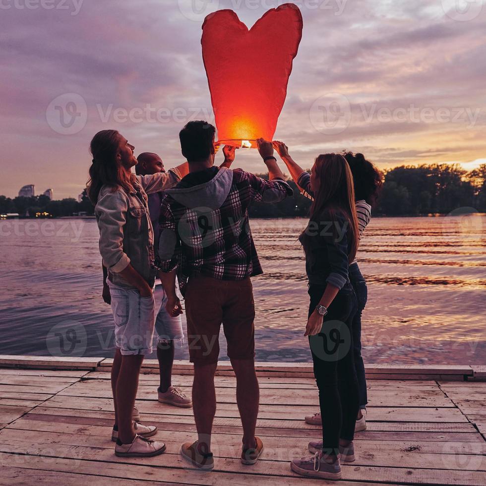 Fun with friends. Full length of young people in casual wear preparing sky lantern while standing on the pier photo