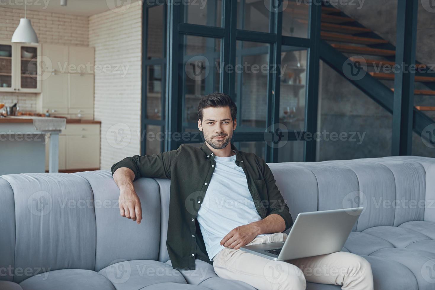 Handsome young man using laptop while sitting on the sofa at home photo