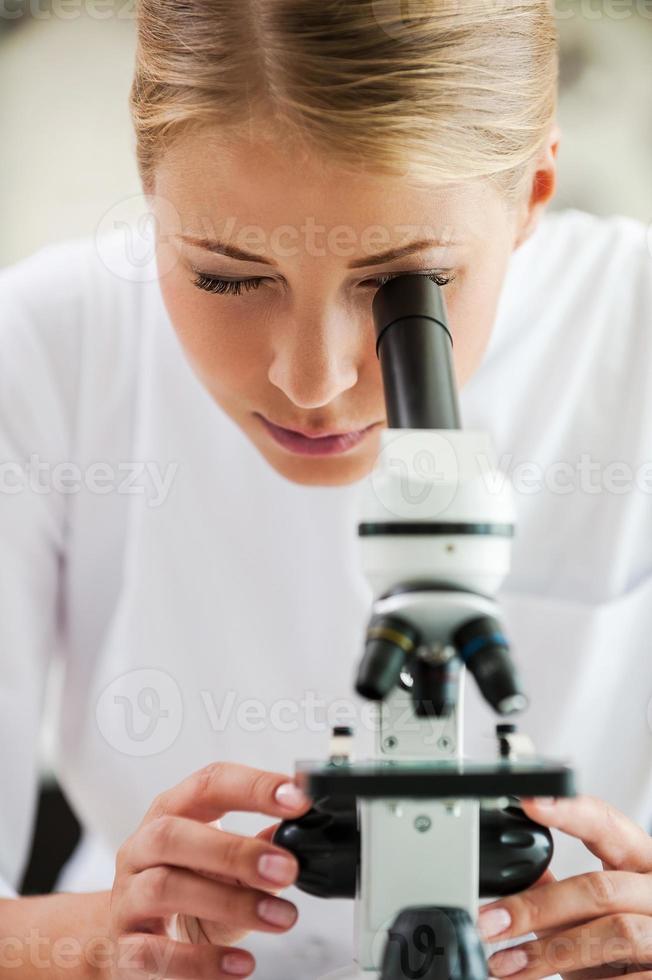 Taking closer look. Concentrated young female scientist using microscope while working in the laboratory photo