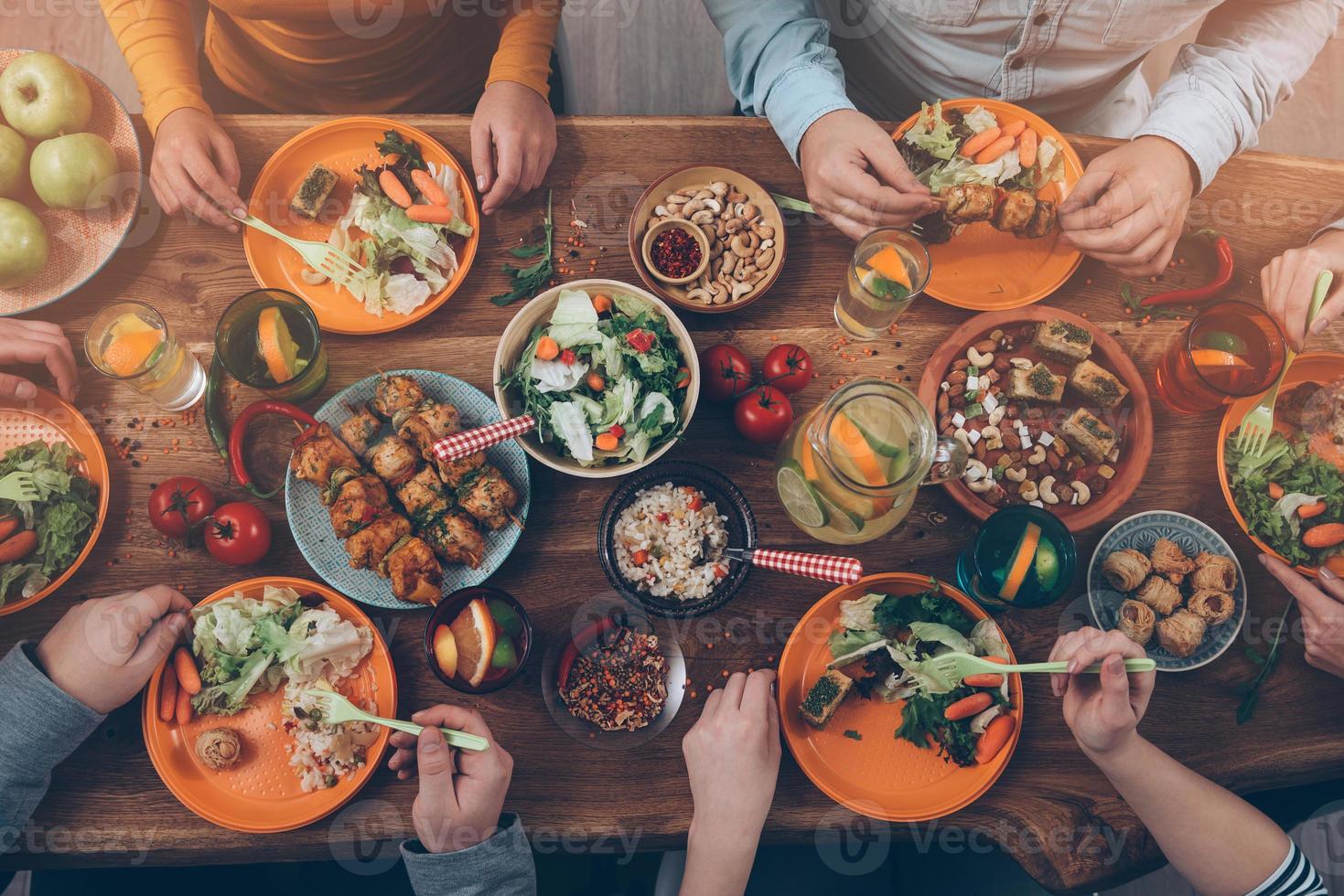 Enjoying dinner with friends. Top view of group of people having dinner together while sitting at the rustic wooden table photo