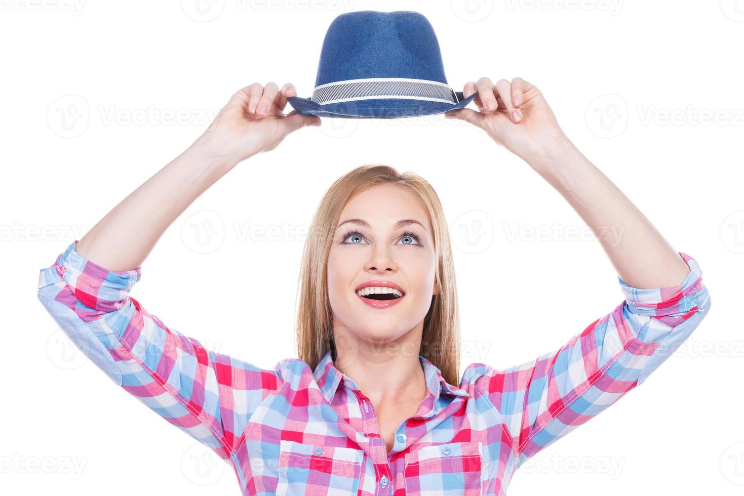My favorite hat Beautiful young woman in funky wear holding her hat upon head and looking at it with smile while standing against white background photo