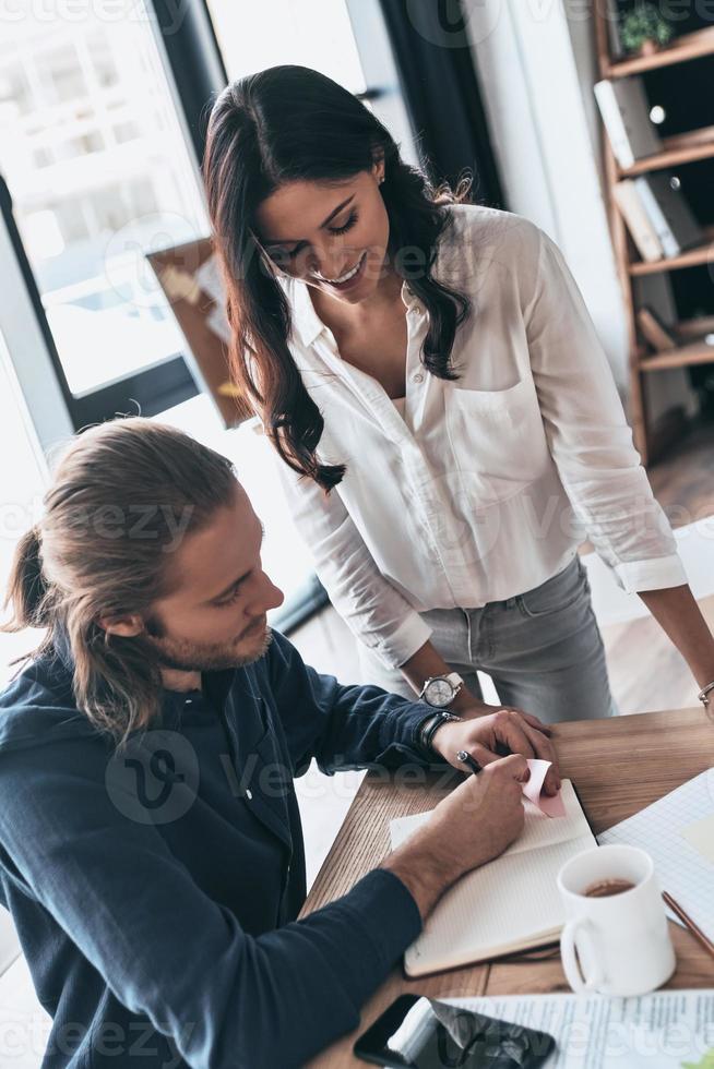 repasando detalles. vista superior de jóvenes colegas modernos con ropa informal inteligente que trabajan juntos y sonríen mientras pasan tiempo en la oficina creativa foto