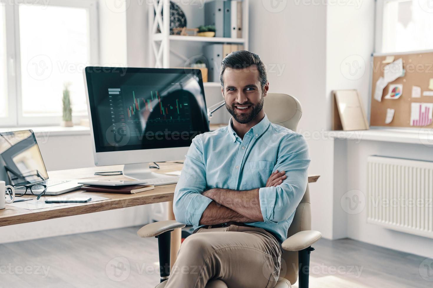 Young and successful. Young modern businessman looking at camera and smiling while sitting in the office photo