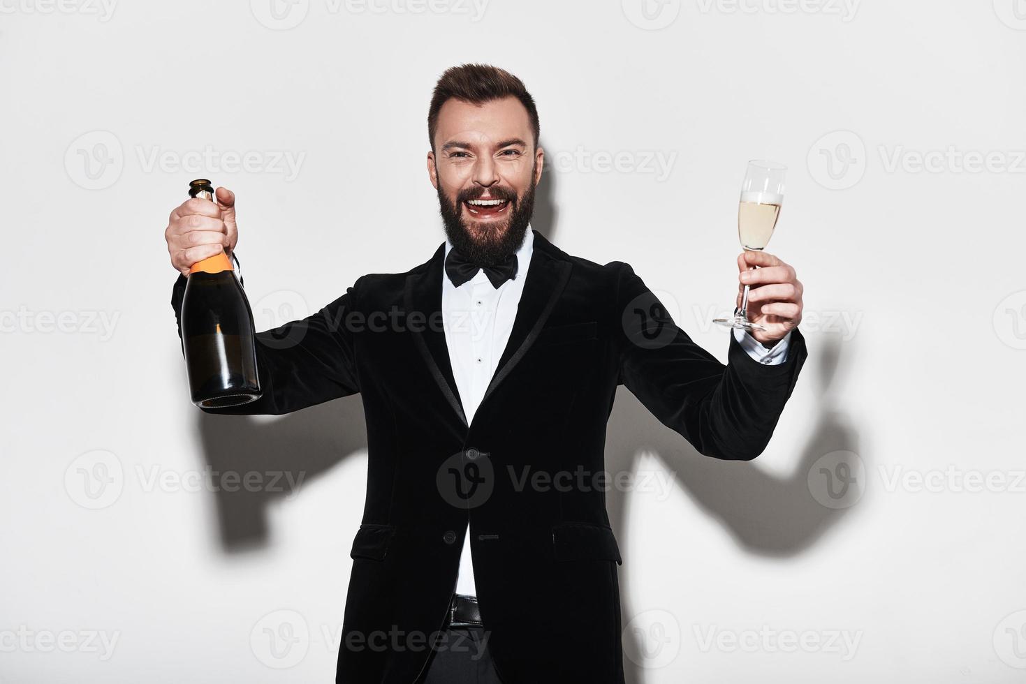 Let the party begin Handsome young man in full suit holding a bottle of champagne and smiling while standing against grey background photo
