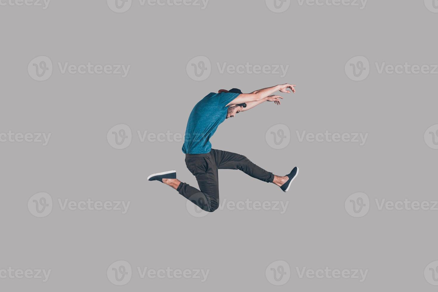 Freedom in moving. Mid-air shot of handsome young man in cap jumping and gesturing against background photo