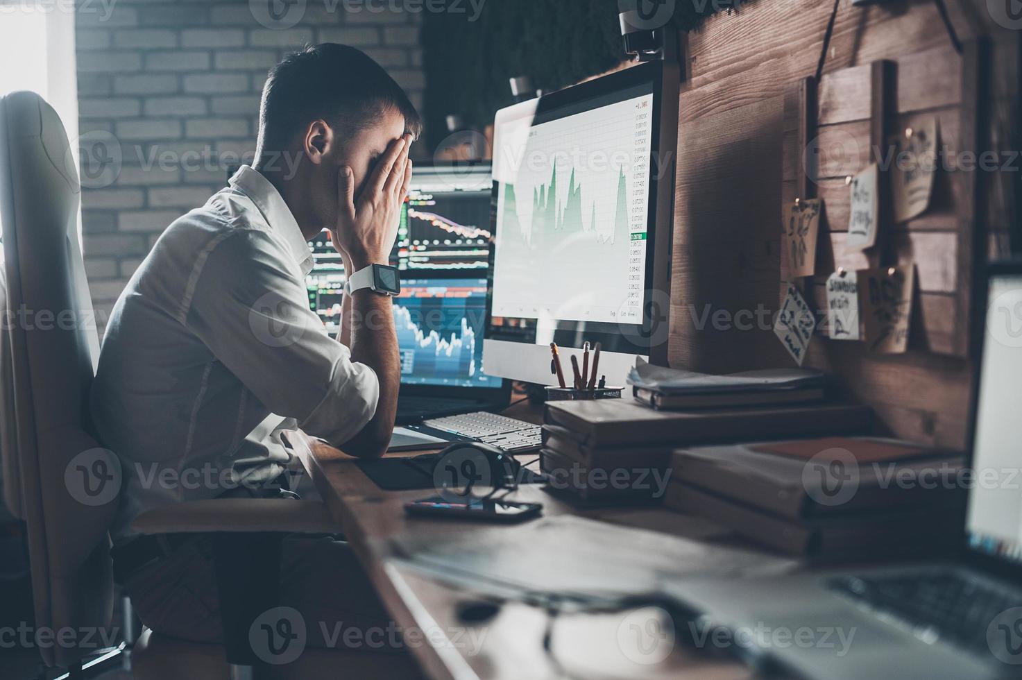 Stressful day at the office. Young businessman holding hands on his face while sitting at the desk in creative office photo