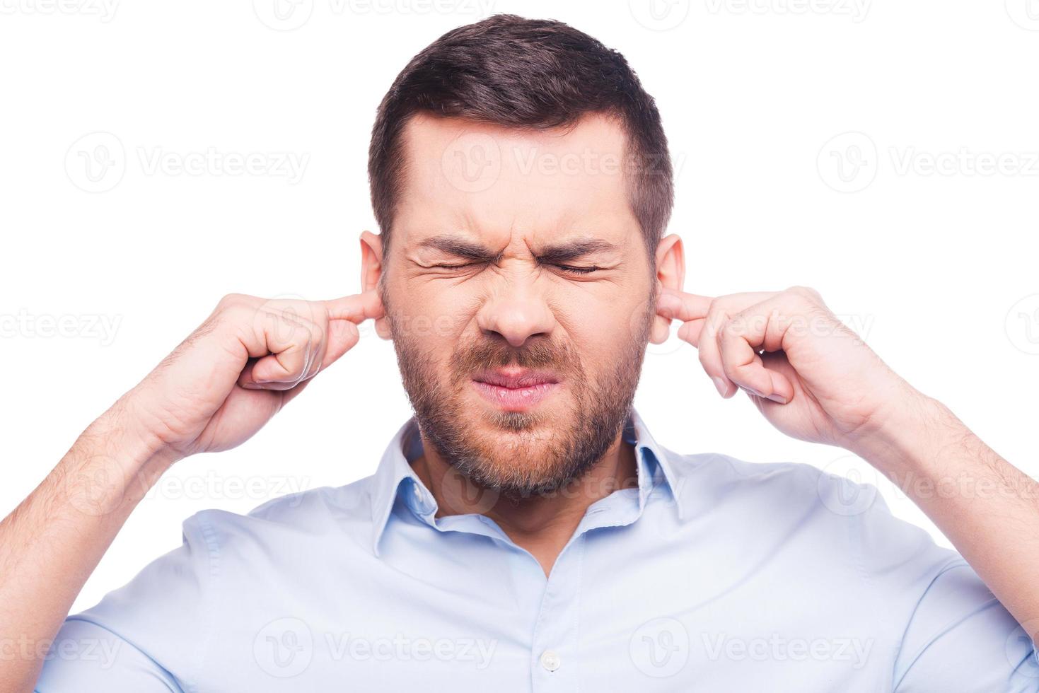 This is too loud Frustrated mature man in shirt holding fingers in his ears and keeping eyes closed while standing against white background photo
