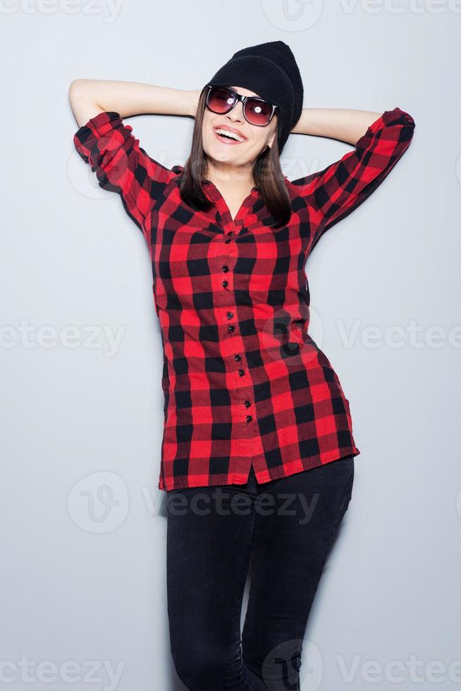 Cheerful and stylish. Attractive young woman in glasses posing and looking at camera while standing against grey background photo