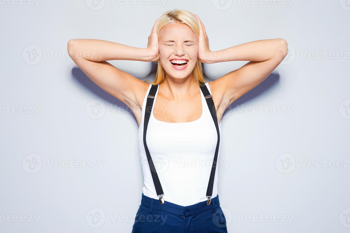 I refuse to hear you. Surprised young woman covering ears with hand and keeping eyes closed while standing against grey background photo