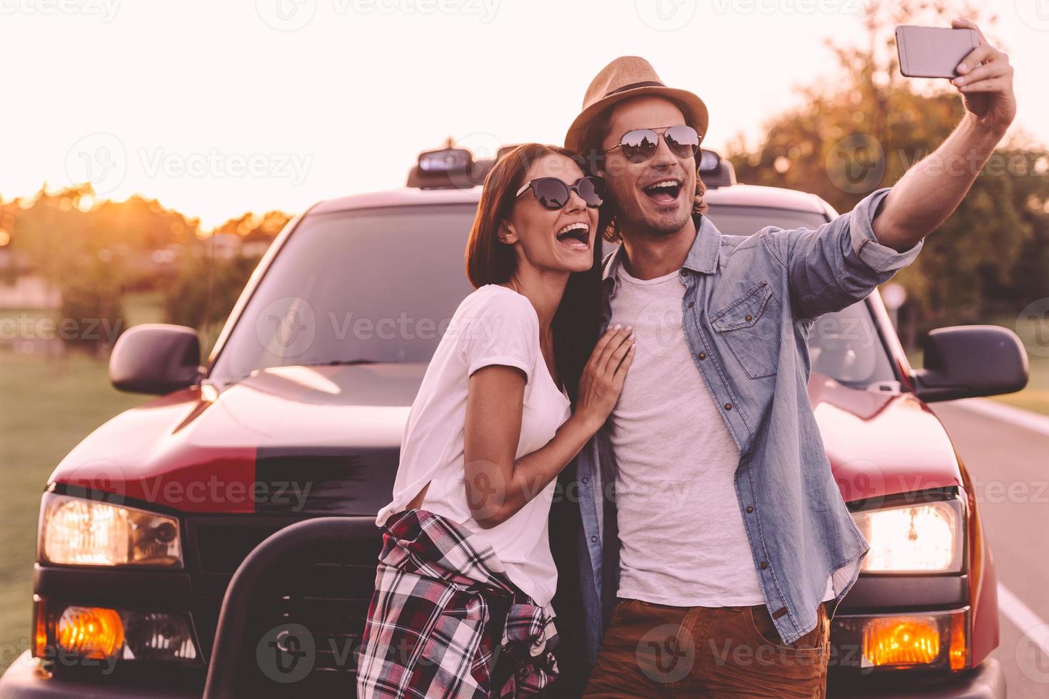 Capturing fun. Beautiful young couple bonding to each other and leaning at their pick-up truck while making selfie photo