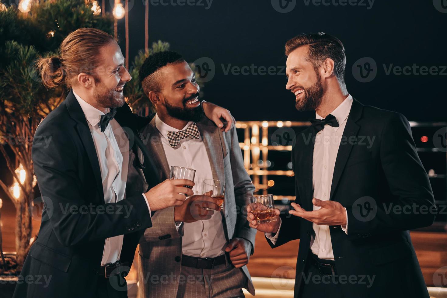 Three handsome men in suits drinking whiskey and communicating while spending time on party photo