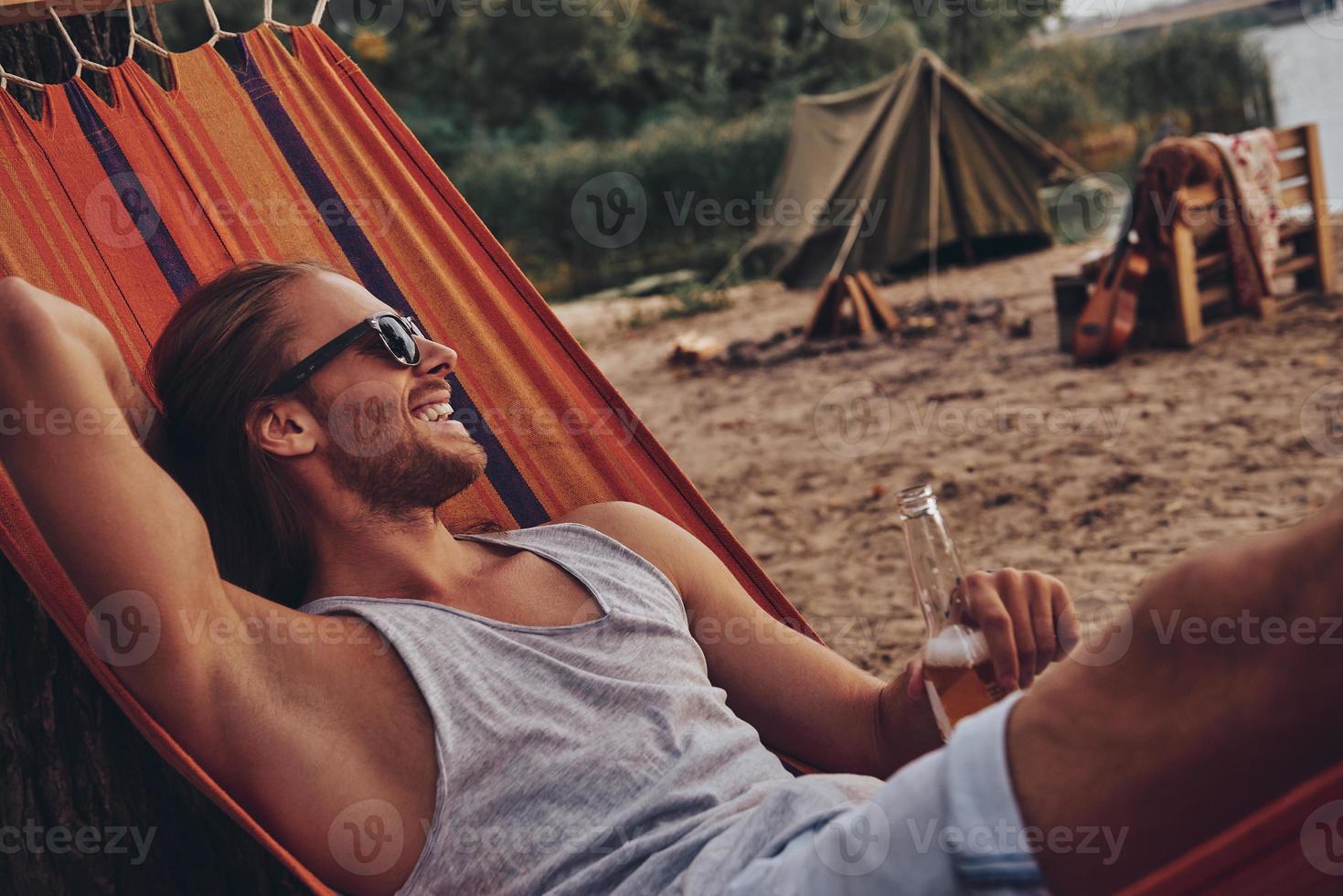 Real relaxation. Handsome young man keeping hand behind head and smiling while lying in hammock photo
