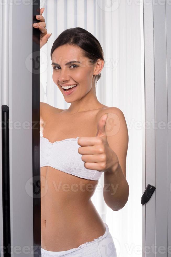 Beauty in solarium. Attractive young woman looking out of tanning booth and gesturing photo