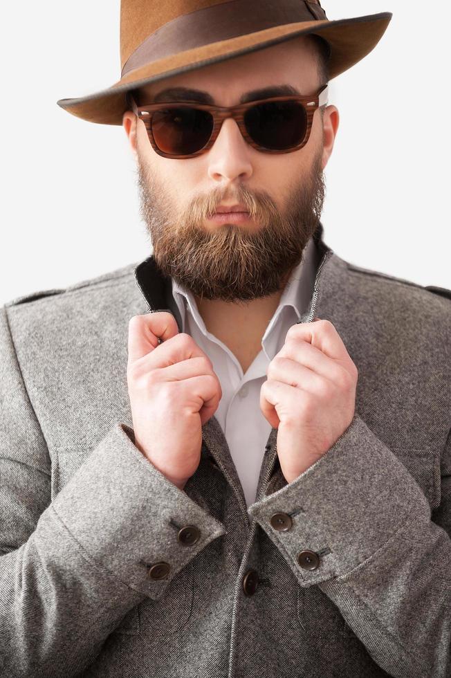 Confident in his handsome look. Handsome young man in formalwear adjusting his coat while standing against gray background photo