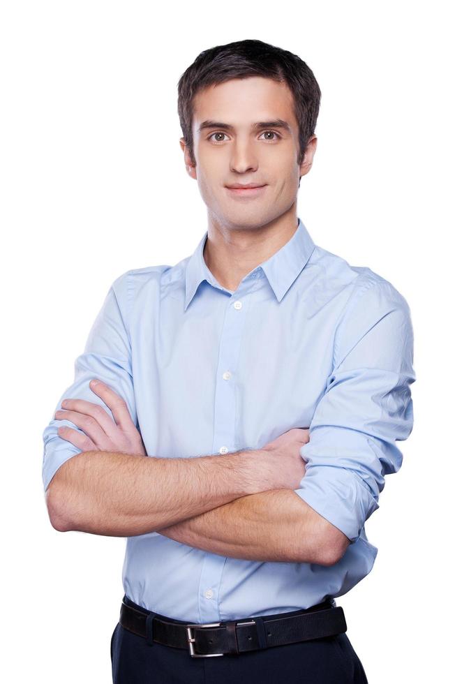 joven y exitoso. un joven apuesto con camisa azul mirando a la cámara y manteniendo los brazos cruzados mientras estaba aislado en blanco foto