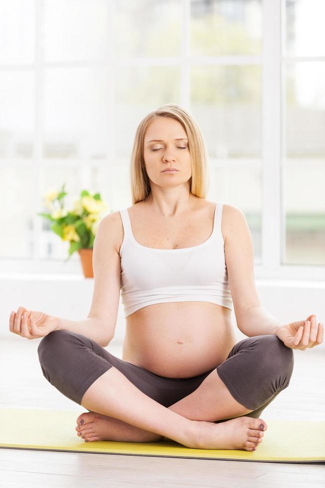 mujer embarazada meditando. hermosa mujer embarazada mediando mientras está sentada en posición de loto foto