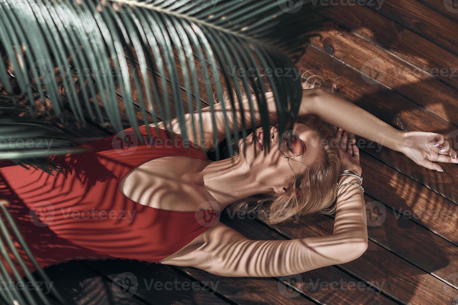 Pure sensuality. Top view of beautiful young woman in swimwear keeping eyes closed while lying under the palm tree photo