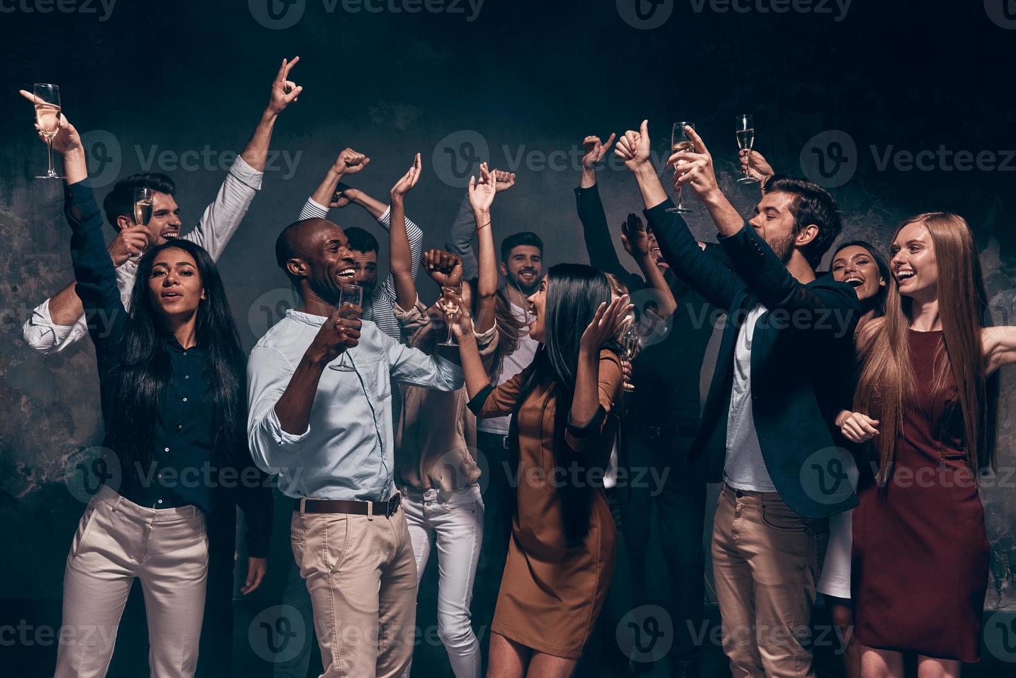 Enjoying amazing party. Group of beautiful young people dancing with champagne flutes and looking happy photo